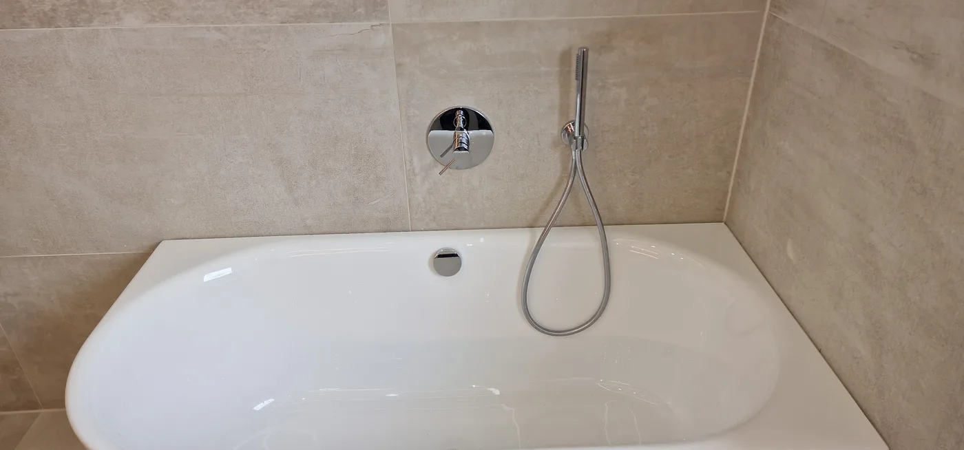 Ein fertig saniertes Bad: neue Wanne mit moderner Armatur und großformatigen Fliesen